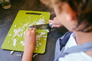 Crop boy chopping fresh onion while cooking in kitchen photo
