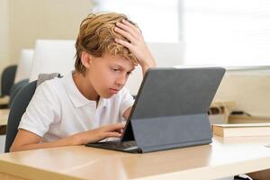 Tired boy using tablet during lesson at school photo