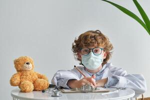 Boy in medical uniform with toy bear during checkup photo