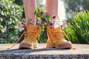 Crop person wearing boots with flowers standing in garden photo