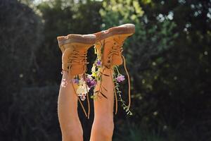 Crop person wearing boots with flowers lying in nature photo