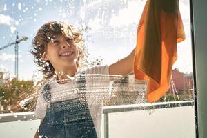 Happy kid cleaning window and smiling photo