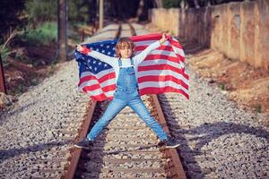 Boy with raised hands and flag of USA on railroad photo