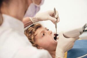 Kid lying on chair with opened mouth while unrecognizable stomatologist treating teeth photo
