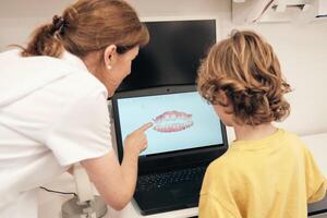 Female dentist explaining 3D teeth scan to faceless boy photo