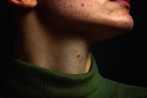 Close-up of a person's neck wearing a green turtleneck, showcasing skin texture and subtle freckles in low lighting photo