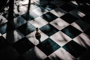 Chess piece standing alone on a checkered board under soft sunlight with shadows creating a dramatic effect photo
