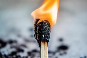 Burning matchstick creating a bright flame on a blurred background of ashes, representing fire and light photo