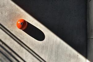 Bright orange object casts a dramatic shadow on concrete. photo