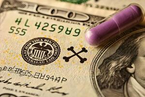 Colorful capsule rests atop a hundred dollar bill in a tense juxtaposition. photo