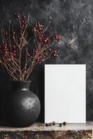 Elegant rustic display featuring black vase and blank canvas with red berries. photo