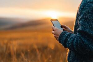 Sunset warmth envelops a figure holding a smartphone amidst golden fields in the early evening glow photo