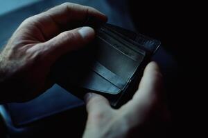 Hands gently open a sleek wallet revealing empty card slots in a dimly lit setting filled with intrigue and anticipation photo