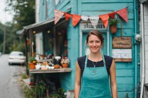 Charming cafe owner smiles warmly in front of vibrant teal building decorated with colorful banners in a small town photo