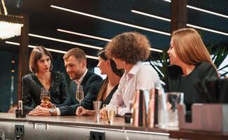 Sitting by ,the bar table. Group of people in beautiful elegant clothes are celebrating New Year indoors together photo