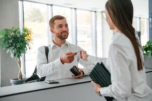 Assistant helping customer. Man in ,white shirt is ordering a room in the hotel by woman's help photo