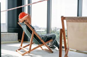 Foreman, in hard hat and uniform is sitting, looking at the view through windows while resting photo