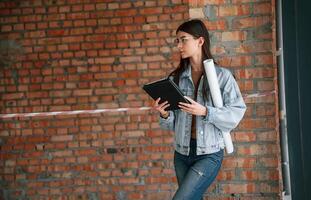 Notepad in hands. Young woman is standing in the, unfinished building on construction site and working on a project photo
