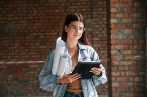 With plan in hands. Young woman is standing in the .unfinished building on construction site and working on a project photo