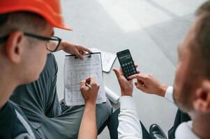 Sitting, using calculator. Manager with foreman are, working on the construction site together photo