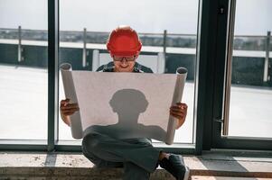 Foreman ,in hard hat is sitting indoors and reading plan of the building and construction photo