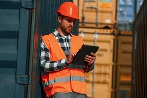 With digital tablet ,in hands. Male worker is on the location with containers photo