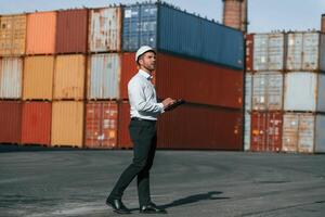 With, digital tablet in hands. Male worker is on the location with containers photo