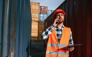 Having, conversation by phone. Male worker is on the location with containers photo