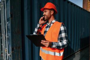 Having conversation, by phone. Male worker is on the location with containers photo