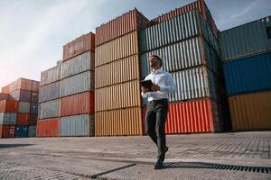 Controlling the process. Holding digital tablet. Male, worker is on the location with containers photo