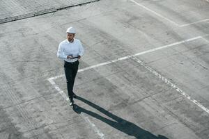 Top view of man in formal clothes and in white hard, hat that is walking with tablet in hands photo
