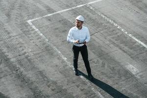 Top view of man in formal clothes and in white hard hat that is walking with tablet in hands photo