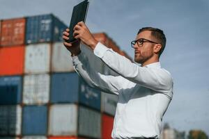 Taking photos by using tablet.. Male ,worker is on the location with containers