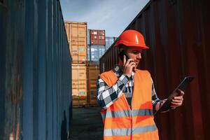 Having conversation by phone. Male worker is on the location with containers photo