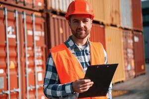 Standing with, tablet in hands. Male worker is on the location with containers photo