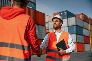 Greetings, handshake. Two male workers is on the location with containers photo