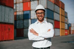 Standing ,with arms crossed.. Male worker is on the location with containers photo
