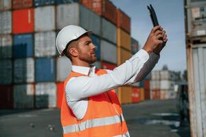 Taking photos by using tablet. Male worker is on the location with containers