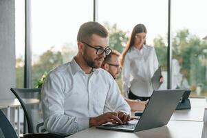 Sitting ,by laptop. Three people in formal clothes are working in the modern office together photo