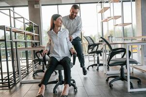 Having fun by riding the chair. Man, and woman are working in the modern office together photo