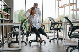Having fun, by riding the chair. Man and woman are working in the modern office together photo