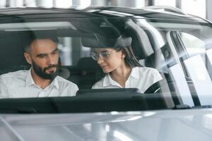 Woman sitting i,n the automobile. Man in white clothes are in the car dealership photo