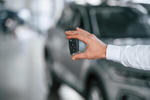 Close ,up view of keys. Young man in white clothes is in the car dealership photo