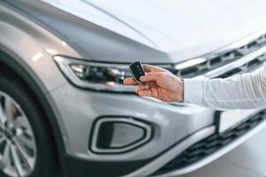 Close up view of keys. Young man in white clothes,is in the car dealership photo