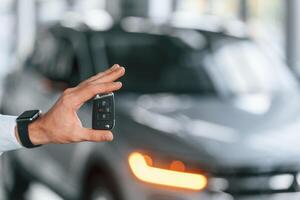Using the keys ,remote controller. Young man in white clothes is in the car dealership photo
