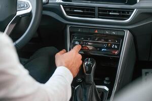 Using the radio. Young man in white clothes is in the car dealership photo