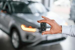 Close ,up view of keys that are in hand. Young man in white clothes is in the car dealership photo