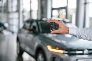 Closing ,the automobile by remote keys. Young man in white clothes is in the car dealership photo