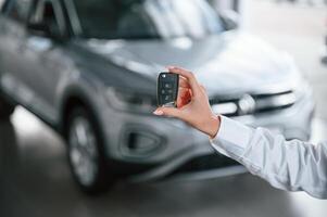 Close up view ,of keys.. Young woman in white formal clothes is in the at dealership photo
