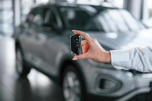 Close up view of keys.. Young ,woman in white formal clothes is in the at dealership photo